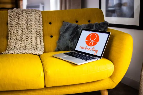 Żółta kanapa z laptopem otwartym na stronie couchsurfing. Obok koc i szara poduszka.